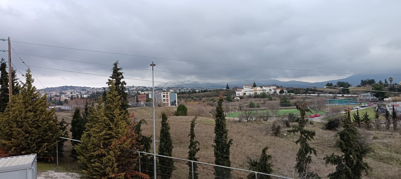 An image of rural landscape with scattered buildings, trees, and a fenced area. Hills and a small town are visible in the background. An image of rural landscape with scattered buildings, trees, and a fenced area. Hills and a small town are visible in the background.