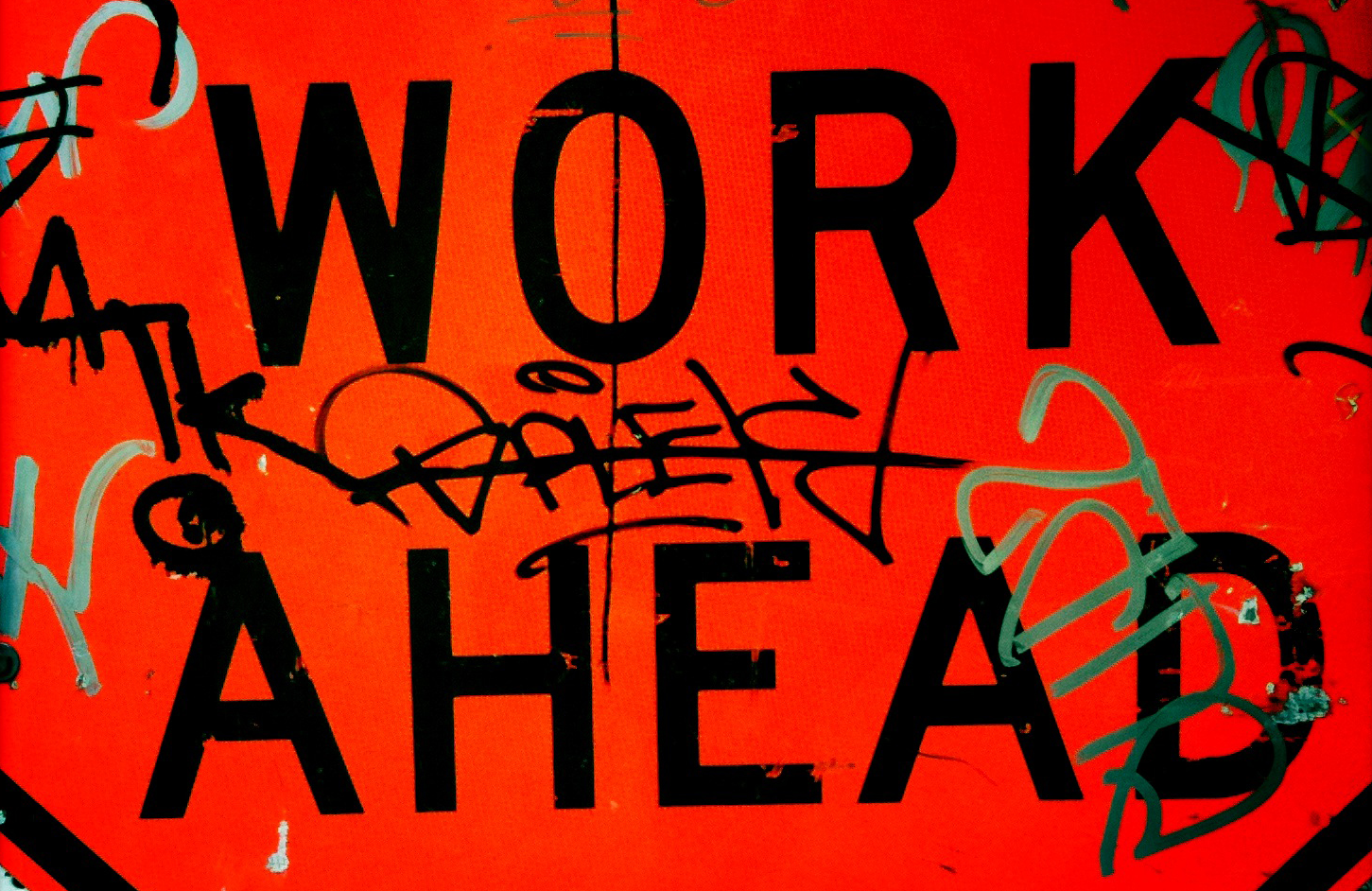 words "WORK AHEAD" displayed on a red background covered in colourful graffiti